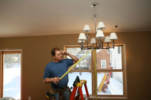 Electrician measuring and thinking while installing luxury chandelier on a home remodel job.