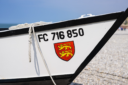 Yport, France - July 21, 2022: The front of a small white fishing boat lying on the beach of Yport, sunny day in summer, red coat of arms