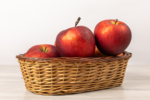 Red ripe apples in a wicker basket on wooden boards.