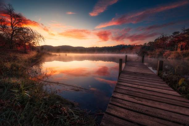 istock Wooden dock extending out into a scenic river, surrounded by lush green trees at sunset 1824438416