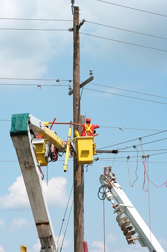 Electricians carefully attach high voltage electrical power lines to a newly installed post.