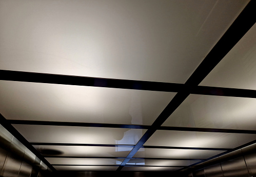 the ceiling of the elevator or corridor is made of plexiglass with top lighting. the ceiling is light and shaped like a square grid, soffit