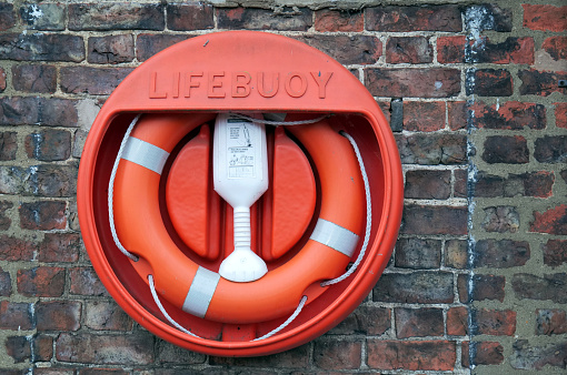 A bright orange and white lifebuoy is hung in its case against an old brick wall