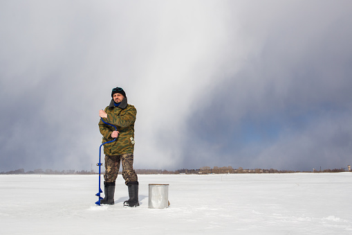 A real fisherman drills a hole in the ice with a drill.