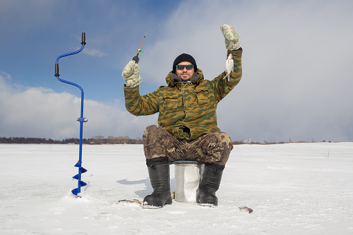 The fisherman rejoices in the caught fish on the ice of the lake.