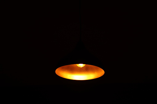 A Black metal bowl pendant spot light illuminated by yellow filament led lights in complete darkness