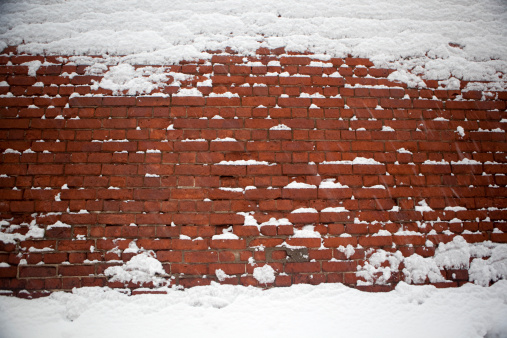 and old brick wall catches snow on it's old leaning brickwork