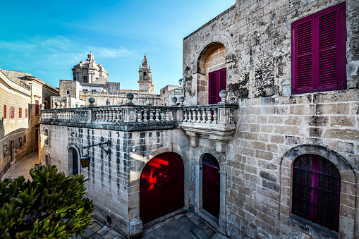 Red Doors And Windows Of Buildings Behind St. Paul's Cathedral In Mdina, Malta