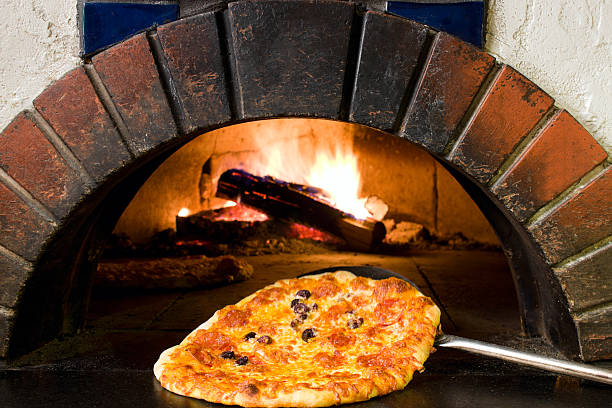 Fresh pepperoni and olive pizza coming out of a wood burning pizza oven.