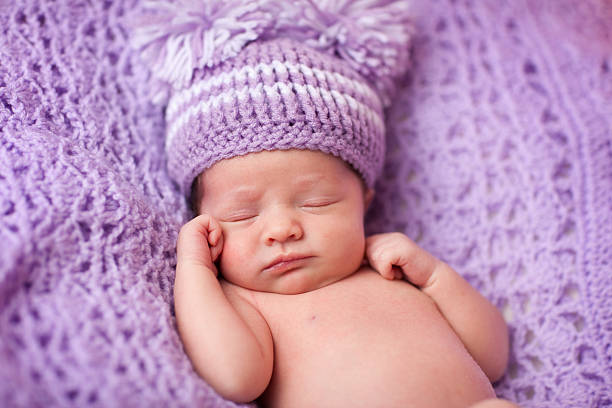 Newborn Baby Girl Wearing Knit Hat Sleeping on Purple Blanket stock photo