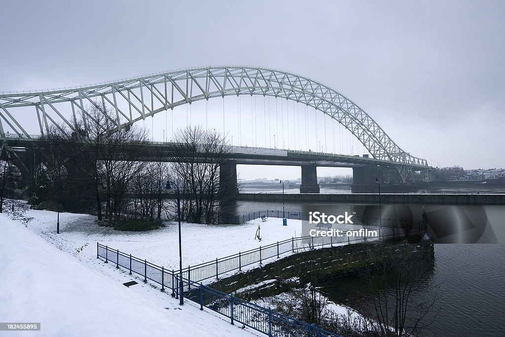 Arch bridge and promenade in winter snow "The Silver Jubilee Bridge at Runcorn Gap, Cheshire, UK, a local landmark. The arch bridge connects Runcorn and Widnes. Snow covers the promenade, and heavy snow clouds overhead. The water in the foreground is the Manchester Ship Canal, with the River Mersey behind the dividing wall." Snow Stock Photo