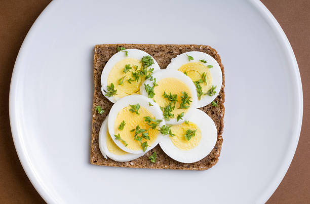 Sliced bread arranging on a wooden cutting board next to a glass bowl filled with brown eggs.