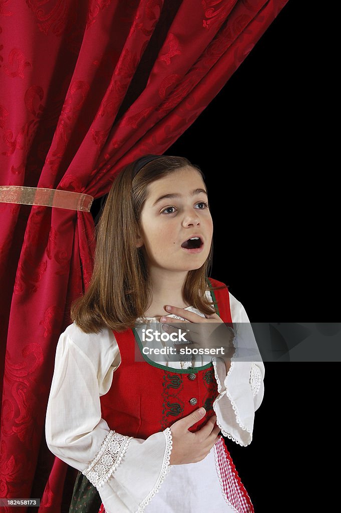 A little girl in her costume in Dirndl singing "A pretty girl wearing an authentic Austrian dirndl, singing dramatically in front of a red stage curtain.More images from this series:" Child Stock Photo