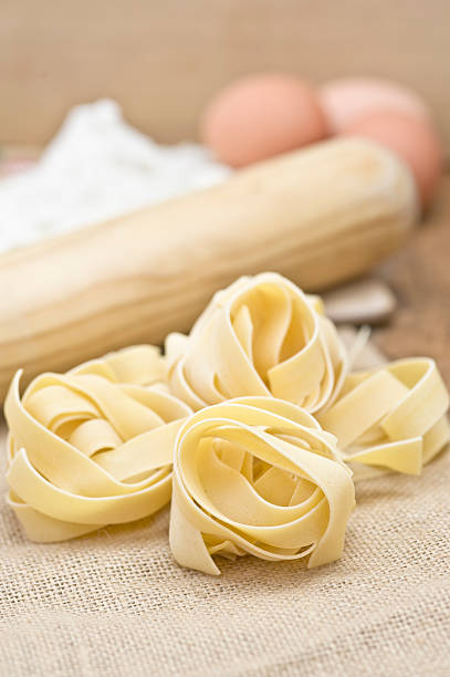 Fettucini pasta, eggs, flour on wood and sack cloth stock photo