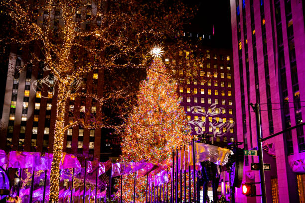 Roclefeller Center Christmas Tree 2023 at night A beautiful illuminated Christmas tree in Rockefeller Center at night with the bright crystal star on top and adorned in lights and ornaments surrounded by the skating rink flags blowing in the night wind rockefeller ice rink stock pictures, royalty-free photos & images