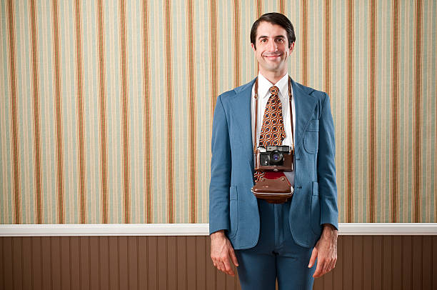 Smiling nerdy tourist in a blue retro suit and  vintage camera. The wall has a brown beadboard wainscoting and a striped wallpaper.Take a look at my LIGHTBOXES of other related images.