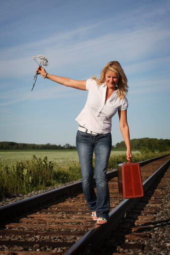 Happy mature woman with a suitcase walking in equilibrium on a railroad track