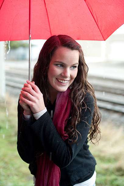 Woman hides from rain under umbrella stock photo