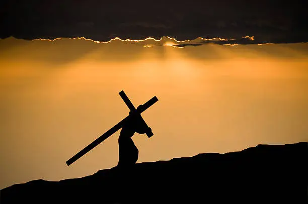 The figure of Jesus Christ carrying the cross up Calvary on Good Friday. The sky is dark and ominus.