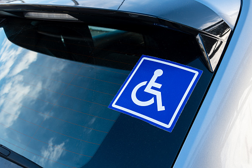 Blue sticker on the rear window of a car with a white pictogram representing a disabled person in a wheelchair. Concepts of transport and mobility of people with disabilities