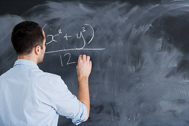 Friendly confident post graduate student standing clutching a folder of class notes with his back to a blank blackboard with copy space