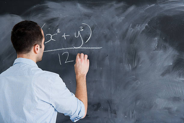 Male teacher writing an algebraic equation on a chalkboard stock photo