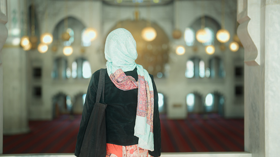 A multiracial female tourist is visiting and walking in a mosque.