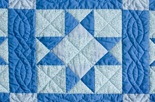 Hand quilted shades of blue cotton. Stitched into star pattern blanket. Horizontal.