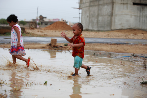 2 year old boy and 3 year old girl are enjoying and playing in a puddle of stranded rainwater.