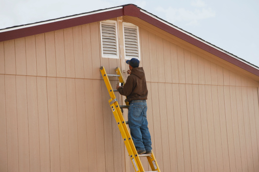 Young Hispanic man painting the seam on a double wide mobile home.