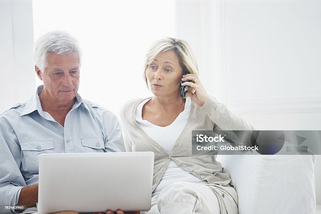 Uomo utilizzando un computer portatile mentre signora parlando sul cellulare - Foto stock royalty-free di Serio