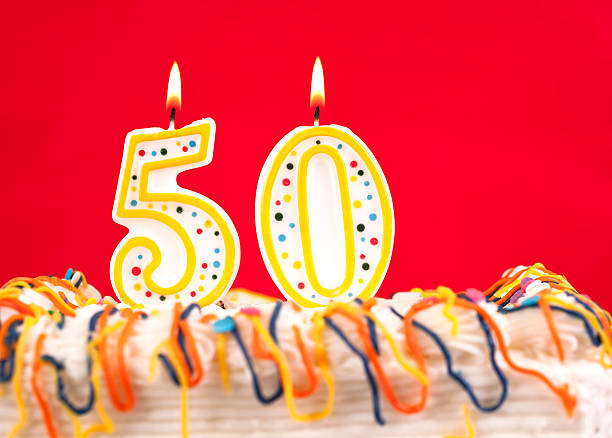 istock Decorated birthday cake with number 50 burning candles. Red background. 182464229