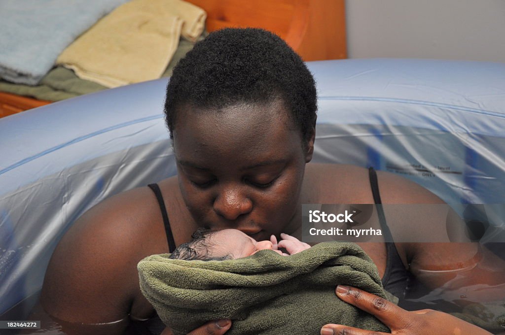Baby-Day; water birth, mother kissing newborn still enjoying the relaxing affects of warm water, newly arrived baby girl is adored by her mom Water Birth Stock Photo