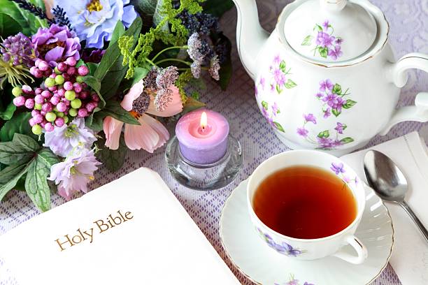 Lovely teapot and tea cup with violets with Bible, candle and flowers ready for meditation time. 
