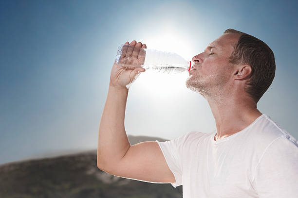 Hot sunny day drinking water from a bottle Hot sweaty man quenches thirst with bottled water. quench your thirst pictures stock pictures, royalty-free photos & images