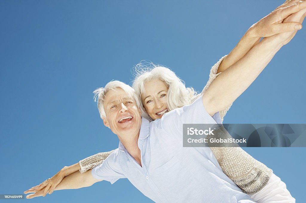 Coppia Senior stretching loro mani insieme contro il cielo blu - Foto stock royalty-free di 55-59 anni