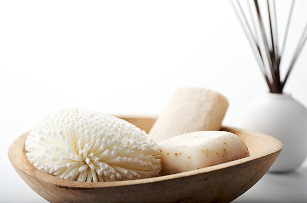 Natural Bath Spa Items Still Life on White Background "A wooden bowl holds a loofah, a flower sponge and soap with aromatherapy diffuser sticks in the background on a white high-key background.  Shallow DOF." loofah photos stock pictures, royalty-free photos & images