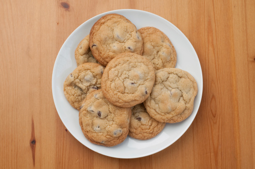 A horizontal image of a plate of freshly baked tasty chocolate chip cookies.  Focus is on the cookie of top. More cookies:
