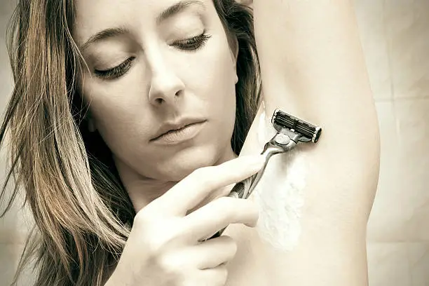 Image of young beauiful woman shaving her armpit.