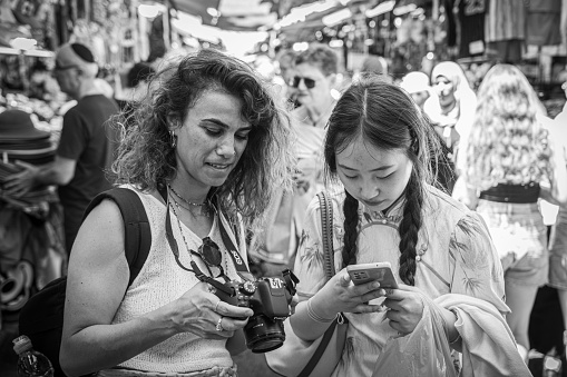 Tel Aviv, Israel – August 04, 2023: The two female friends smiling and looking at a mobile phone while standing side by side