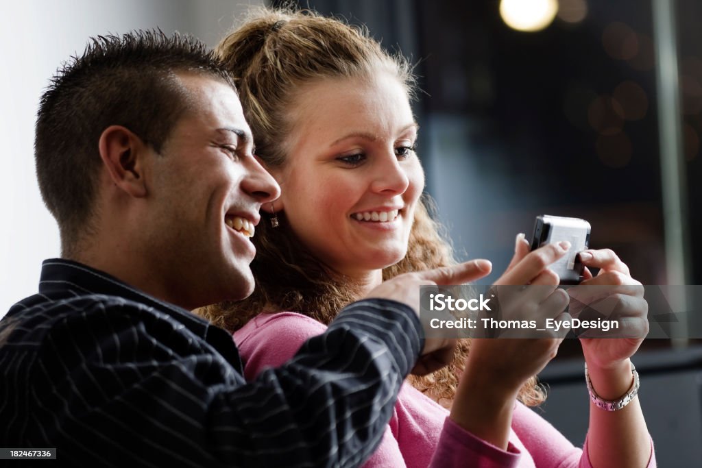 Couple Laughing at Cell Phone Young woman shows funny content on her mobile phone to a young man. He is pointing at the phone's screen. Horizontal shot. 20-29 Years Stock Photo