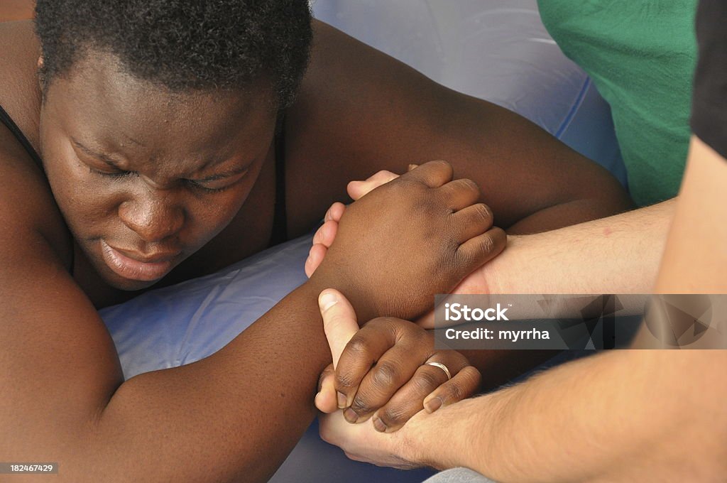 Baby Day~Water Birth Pregnant Black Woman mother-to-be in birthing tub grips husbands hands during delivery Childbirth Stock Photo