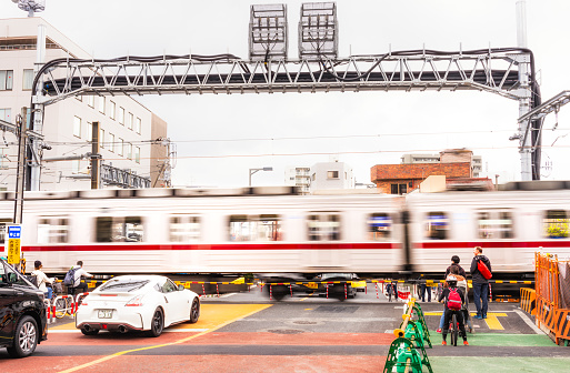 Tokyo, Japan - Pedestrians, cyclists and drivers wait behind the level crossing barrier as a train passes across a street in the Sumida ward of Tokyo.