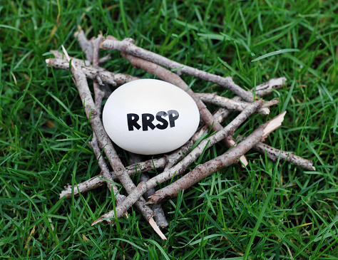 Close up of an egg in a nest of twigs on grass with RRSP written on it symbolizing a RRSP contribution.  See also