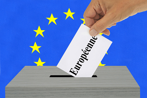 European election concept with a hand putting a ballot paper on which is written Européenne in French language into an electoral box against the background of the European Union flag