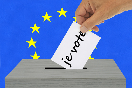 European election concept with a hand putting a ballot paper on which is written in French language I vote into an electoral box against the background of the European Union flag