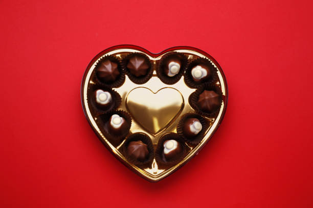 Heart shaped box with delicious chocolate candies on red background, top view