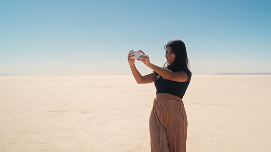A multiracial female tourist is explaring and using her mobile smart phone to take photos and videos in Tuz Gölü Salt Lake in Anatolia region of Türkiye Turkey.