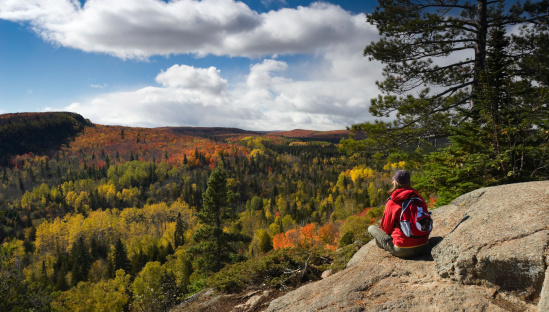 Female hiker sitting on rocky ledge taking in a scenic Autumn view in Minnesota's Arrowhead region from Oberg Mountain.