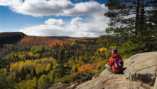 Hiker resting and taking in an Autumn view. Female hiker sitting on rocky ledge taking in a scenic Autumn view in Minnesota's Arrowhead region from Oberg Mountain. minnesota stock pictures, royalty-free photos & images